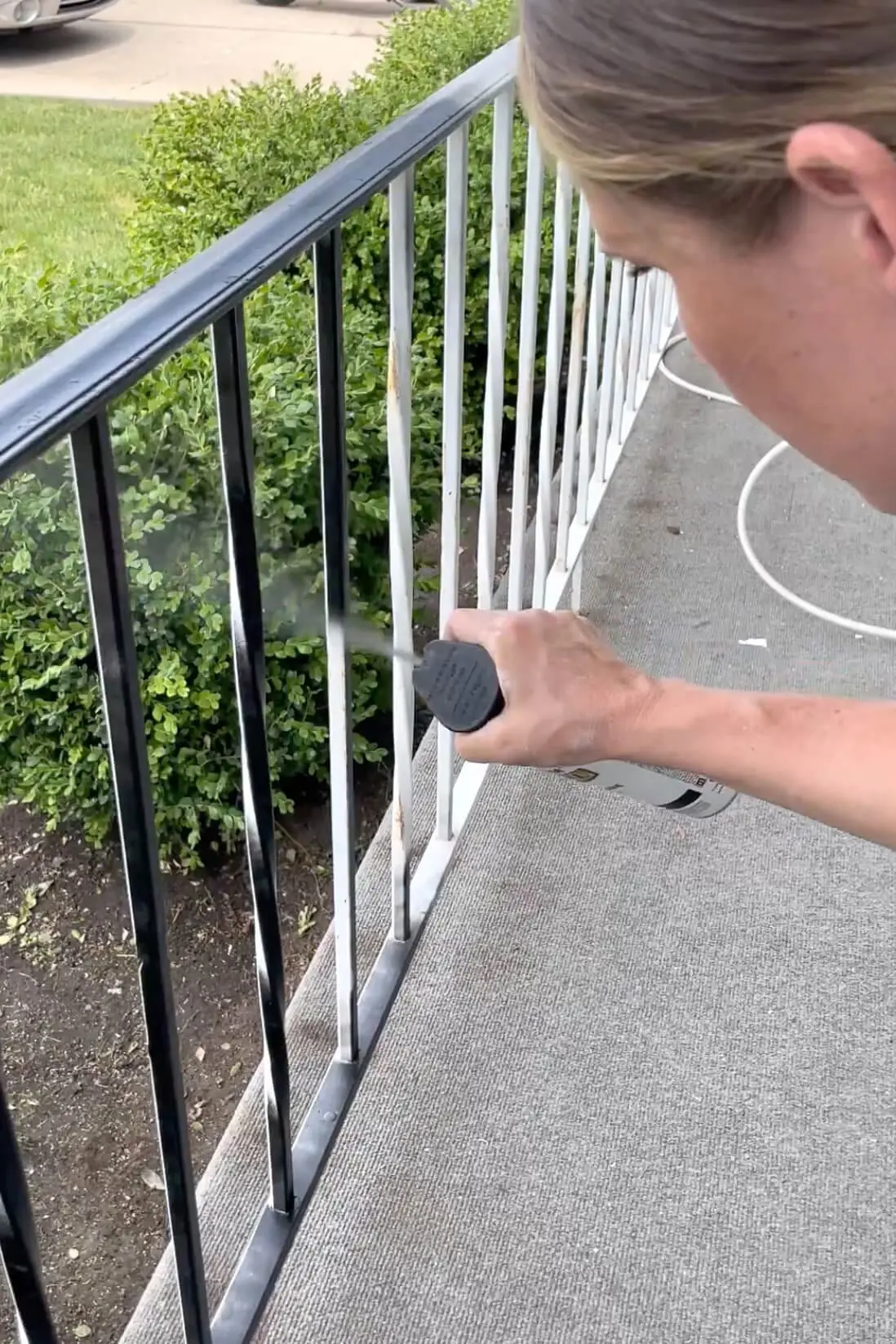 Close-up of a person spray painting white metal railings black during a DIY exterior makeover to refresh the front of the home with a clean, modern look.